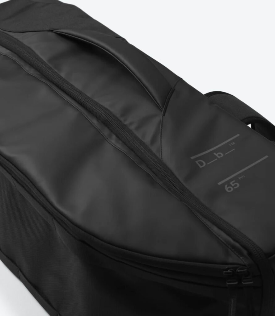 Close-up of the Db Journey Skate Duffel 65L exterior showing the durable black shell, waterproof zipper, and minimalist Scandinavian branding on the travel bag