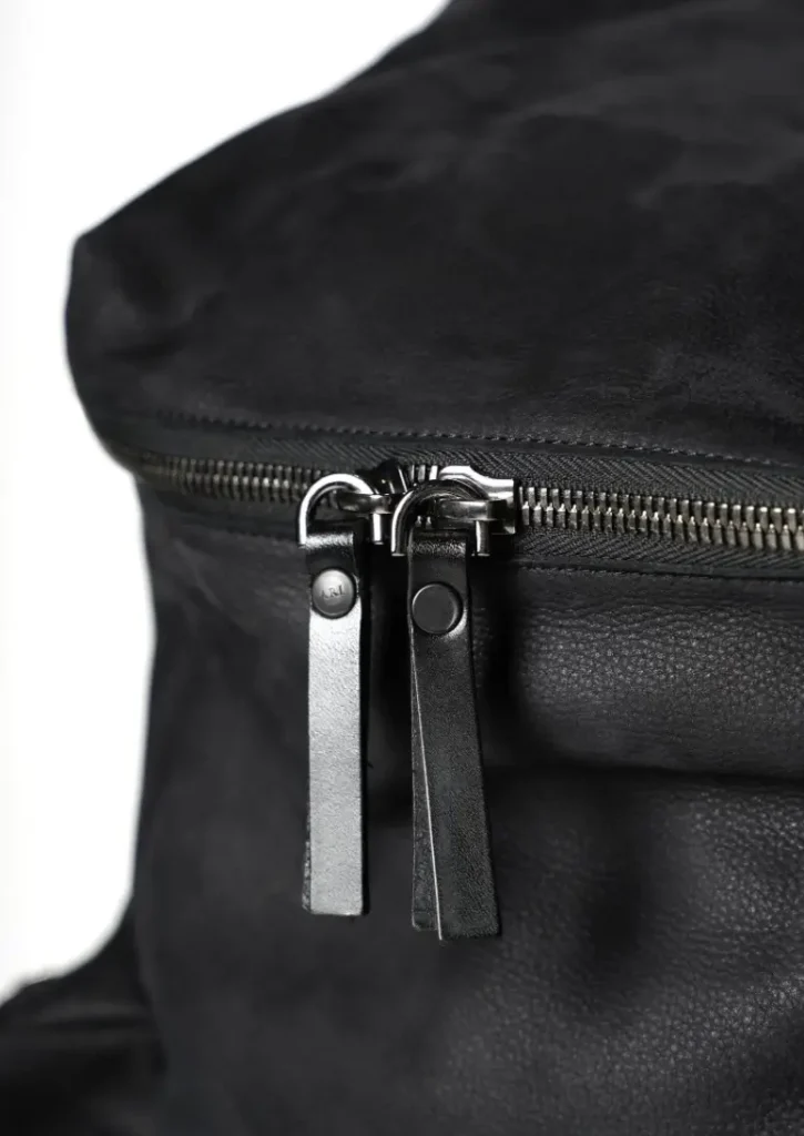 Close-up detail of the Ari Soho ENZO backpack zipper with dual leather pull tabs and black nubuck leather texture