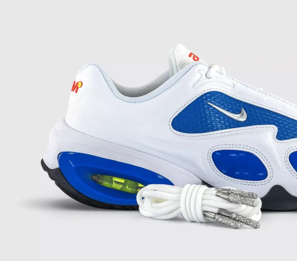 Close-up of the Veneda Carter x Nike Air Max Muse sneaker in white and racer blue, highlighting the metallic silver Swoosh, sculpted midsole with visible volt Air unit, and white rope laces with jewel-like metallic lace tips