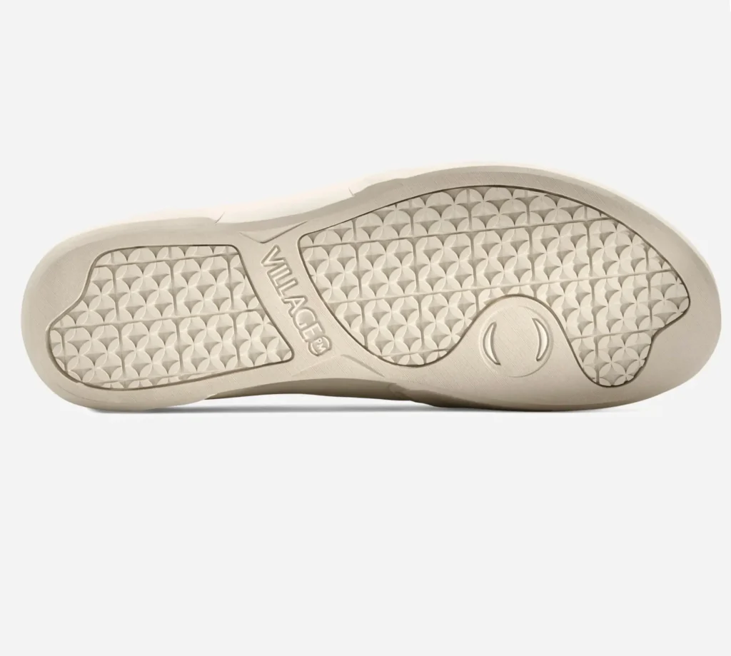 Outsole view of the Village PM 1PM shoe in cream, featuring a textured geometric traction pattern, tonal rubber finish, and subtle VILLAGE PM branding along the midfoot