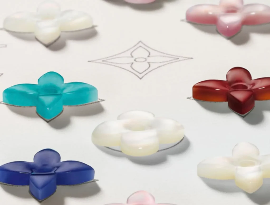 Louis Vuitton Colour Blossom gemstone elements in monogram flower shapes, displayed in sodalite blue, amazonite green, mother-of-pearl white, and pink and amber tones, arranged on a design surface with a central LV motif sketch