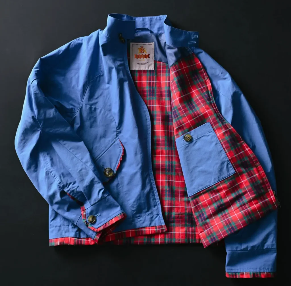 Close-up of BARACUTA x UNDERCOVER blue swing top jacket revealing red tartan lining, interior pocket detailing, and co-branded label from the SS26 “but beautiful 6…” collection