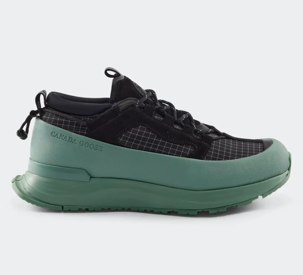 Side profile of the Women’s Glacier Trail Sneaker in Dyneema®, showcasing the black ripstop grid upper, suede-like reinforcement panels, lace system with reflective cords, and a sculpted sage-green midsole with extended rubberized rand and subtle “Canada Goose” branding along the lateral side, designed for lightweight durability and multi-terrain performance