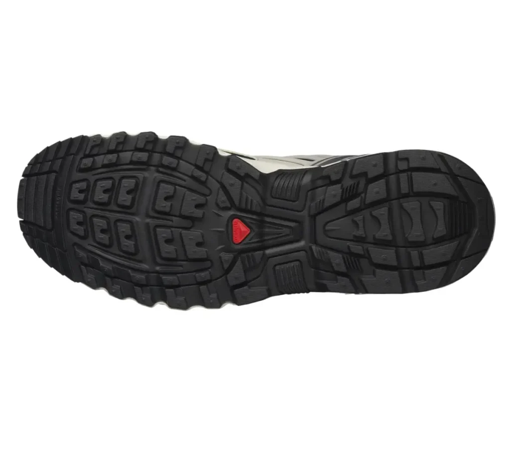 Outsole view of the Salomon ACS Pro Shell sneaker, featuring a rugged black Contagrip tread pattern with multi-directional lugs and a central red stability insert for enhanced traction and control