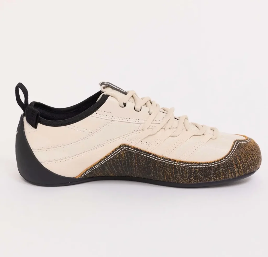 Side profile of the PUMA x GUIZIO Klim Low shoe, featuring a cream leather upper, tonal laces, black heel counter with pull tab, and textured brown overlay wrapping the toe and midfoot along a low-profile sole