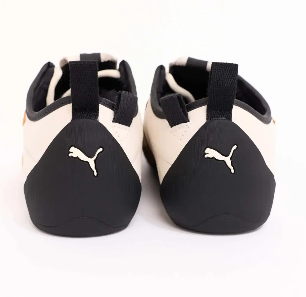 Rear view of the PUMA x GUIZIO Klim Low shoe in cream leather, featuring sculpted matte black heel counters with embossed Puma logos, pull tabs, and a low-profile, minimalist silhouette
