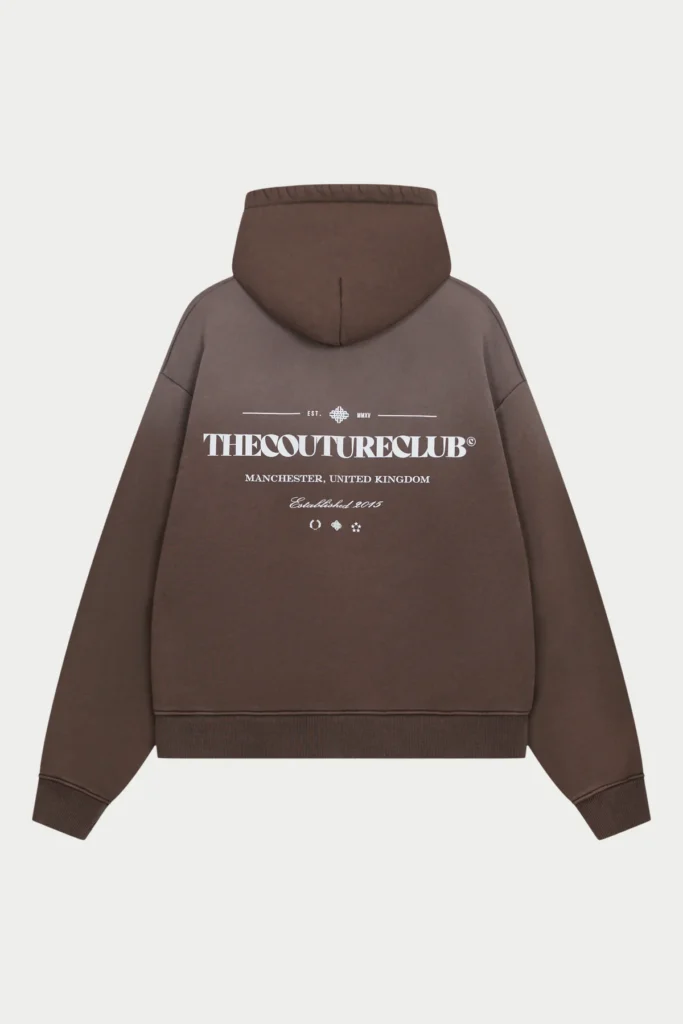 Rear view of a brown The Couture Club hoodie displayed flat, featuring bold white logo typography across the back with “Manchester, United Kingdom” and “Established 2015” detailing, highlighting clean design and relaxed silhouette