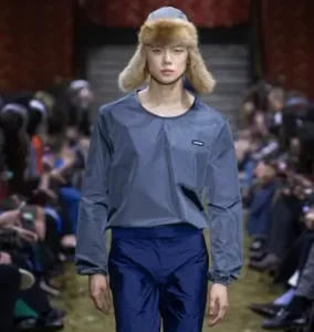 Fashion Week, wearing a gray technical top, navy trousers, and a fur trapper hat