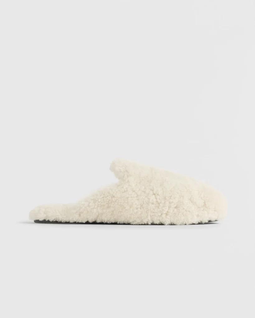 Side profile of cream shearling Tekla slipper, showcasing minimalist slip-on silhouette, plush wool upper, and thin black sole