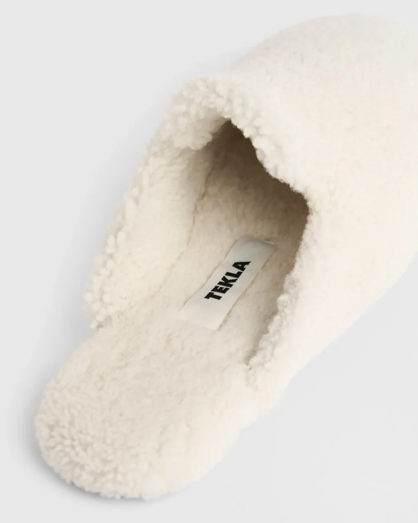 Cream shearling Tekla slipper in angled view, featuring plush wool texture, soft closed-toe silhouette, and minimalist interior with visible Tekla logo tag