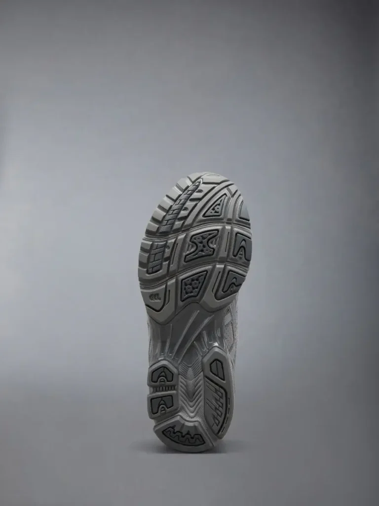 Outsole view of Thom Browne x ASICS GEL-Kayano 14 woven trainers in grey, showing segmented tread pattern, textured rubber grip zones, and visible GEL cushioning structure on a neutral studio background