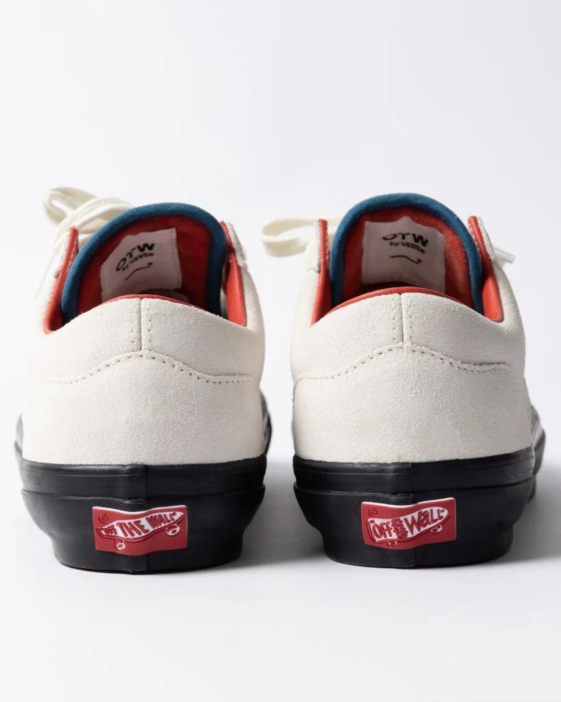 Rear view of Parra x Vans OTW Old Skool 36 “Marshmallow” sneakers in off-white suede, featuring orange inner lining, blue collar trim, black vulcanized soles, and red “Off The Wall” heel tabs, shown in a clean studio setting