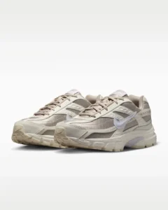 Pair of Nike Initiator sneakers in “Sail Cream” colorway, shown in a three-quarter front angle. The shoes feature breathable beige mesh uppers with layered cream synthetic overlays, a glossy white Swoosh, tonal laces, and a cushioned off-white midsole with subtle gum accents on the outsole