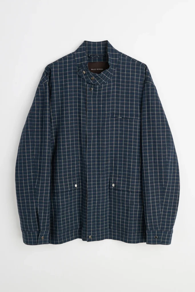 Navy windowpane check jacket from the Wales Bonner Spring Summer 2026 collection featuring a stand collar with snap closure, front placket, chest welt pocket, and flap pockets on a neutral studio background