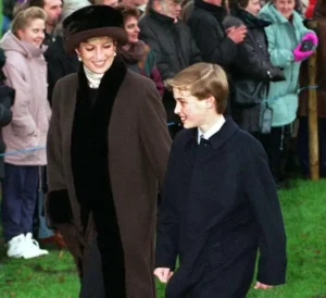 Princess Diana smiles warmly while walking beside a young Prince William during a public appearance, both dressed in dark winter coats as a crowd watches in the background