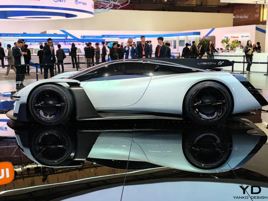 Xiaomi Vision Gran Turismo electric hypercar concept displayed at Mobile World Congress 2026, shown in side profile on a reflective platform with attendees and technology booths in the background