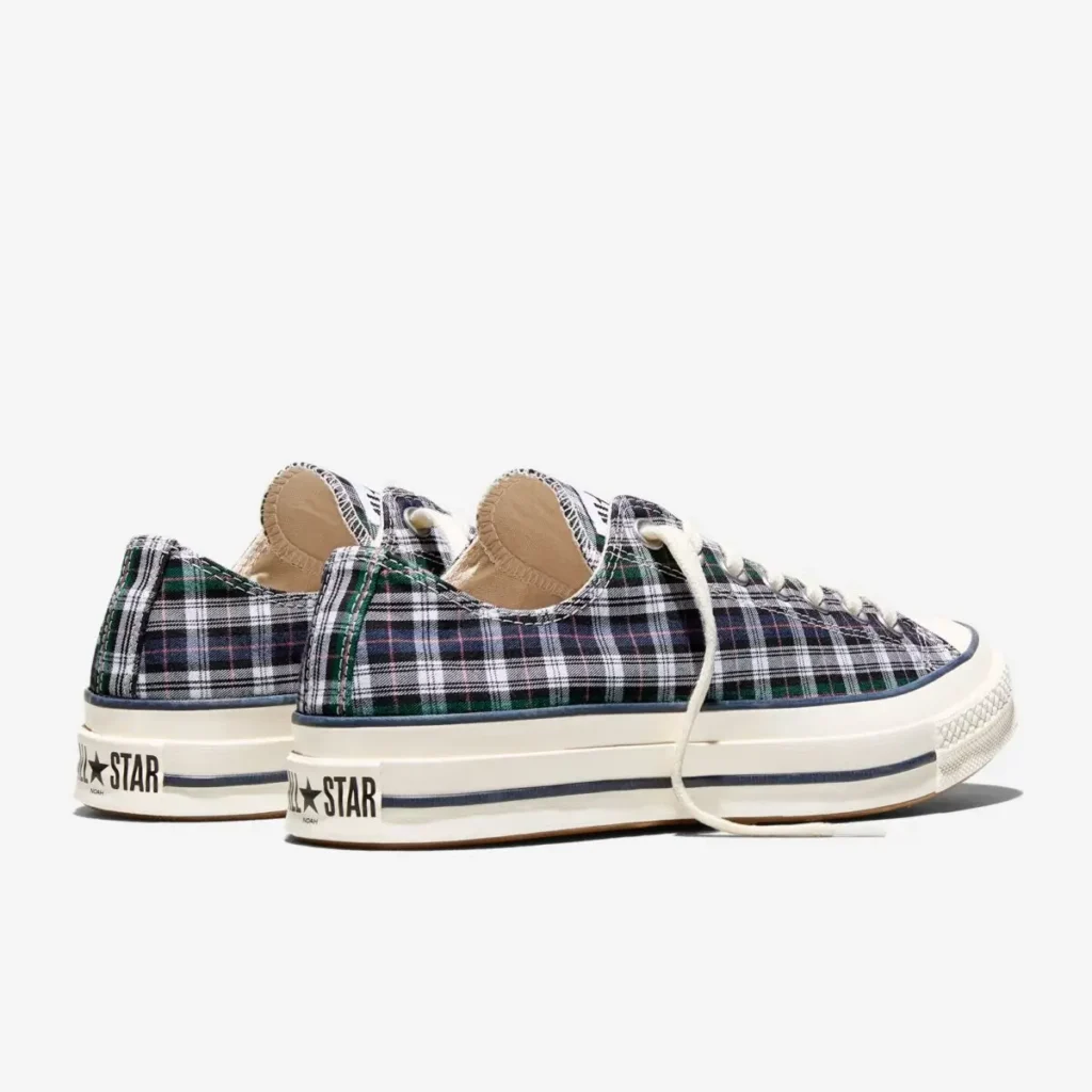Rear three-quarter view of Converse Chuck 70 low-top shoe showcasing a navy, green, and white plaid canvas upper, off-white rubber midsoles with navy stripe, and classic “All Star” heel branding; the paired angle highlights the structured silhouette and understated collaboration with Noah, along with raw-edge detailing around the collar