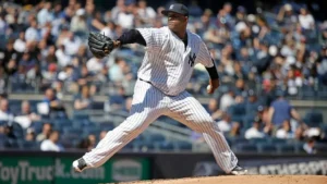 CC Sabathia pitching for the New York Yankees during a game at Yankee Stadium, delivering a powerful throw from the mound in the team’s classic pinstripe uniform with fans visible in the stands behind him
