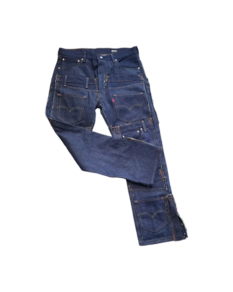 RCNSTRCT Studio Raw Denim Multi Pocket Pant in dark indigo denim displayed in angled front view, featuring layered cargo pockets, reinforced patchwork panels, contrast stitching, and utility-inspired streetwear construction