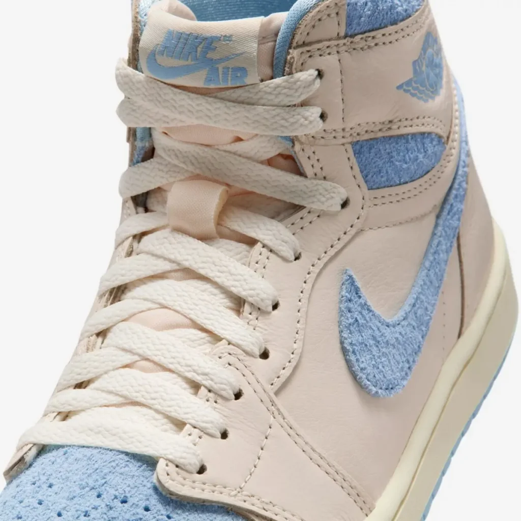 Close-up detail of the Air Jordan 1 High OG WMNS “Psychic Blue” showing cream leather panels, textured pastel blue Swoosh, white laces, and Nike Air tongue branding