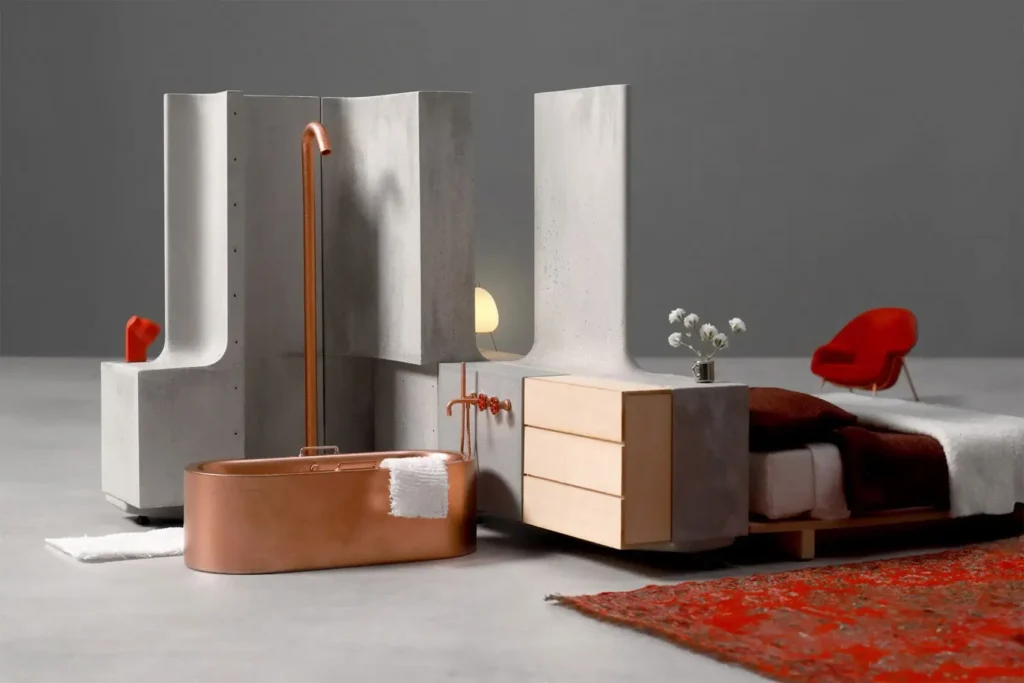Modular concrete components from MIT’s Heirloom House project arranged to form a bedroom and bathroom space with a copper bathtub and minimalist furniture