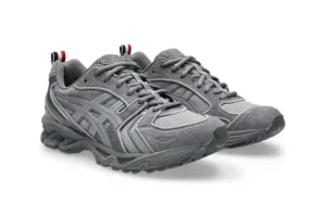 Pair of Thom Browne x ASICS GEL-Kayano 14 woven trainers in grey, featuring layered suede and textile panels, tonal ASICS branding, rugged outsole with visible GEL cushioning, and signature red, white, and blue heel tabs