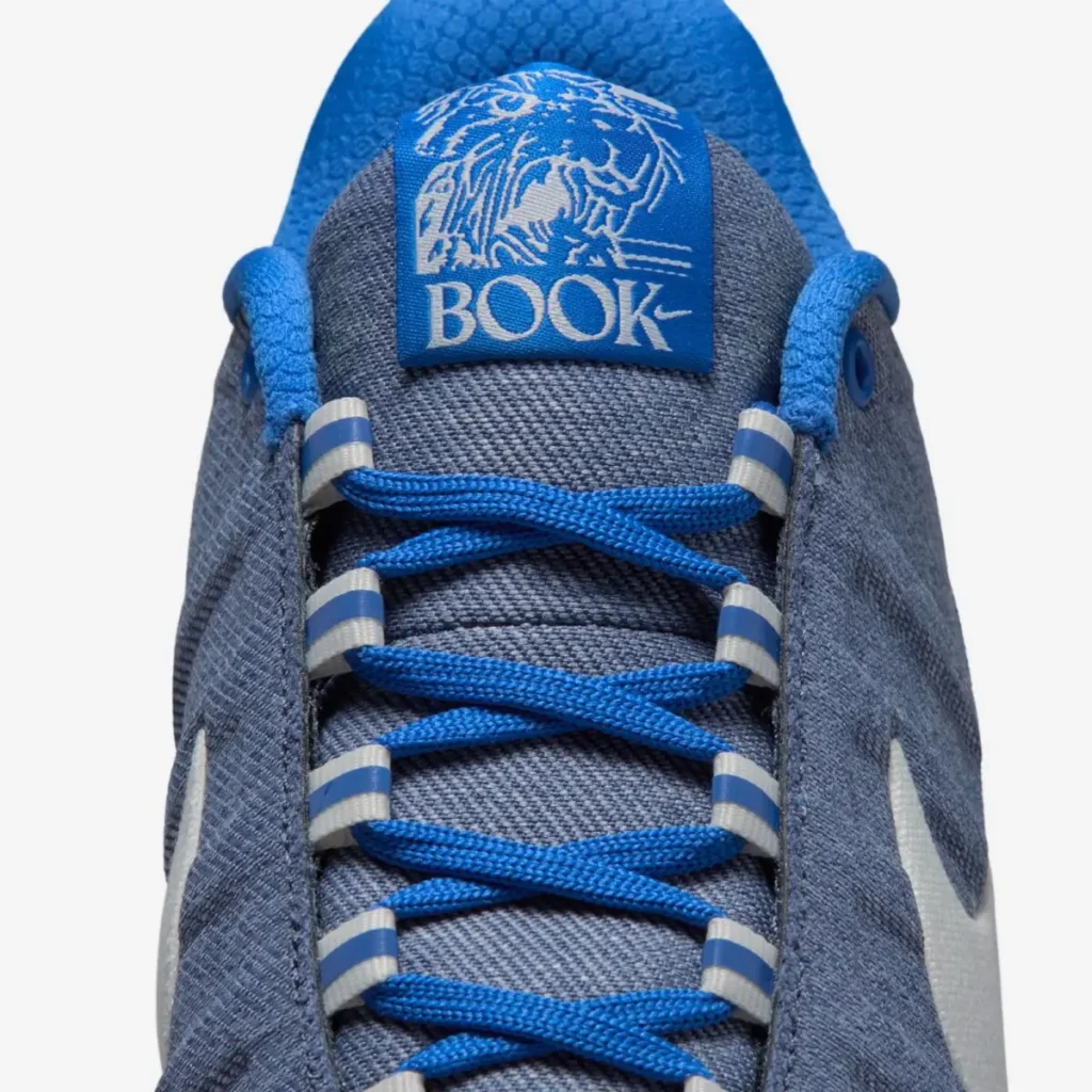 Close-up of the Nike Book 2 “Must Be The Denim” shoe tongue featuring a blue BOOK logo patch with lion graphic, bright blue laces, and denim-textured upper panels inspired by indigo jeans