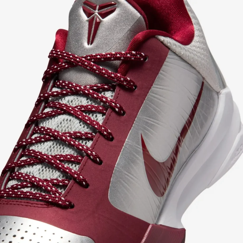 Close-up detail of the Nike Kobe 5 Protro “Lower Merion Aces” showing red patterned laces, metallic silver upper, and glossy red Swoosh inspired by Kobe Bryant’s Lower Merion colors