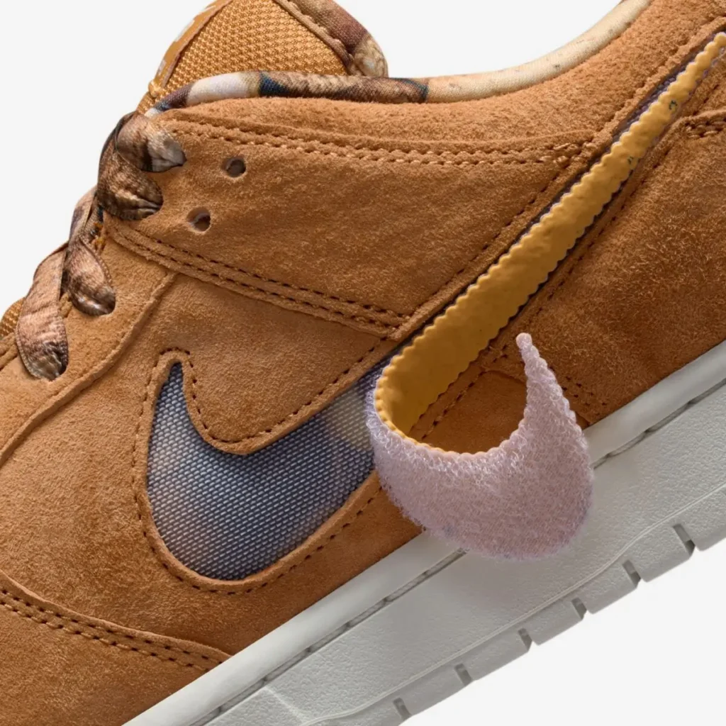 Close-up of NOTE x Nike SB Dunk Low “Brew & Biscuits” showing biscuit-brown suede panels, mesh underlay Swoosh, detachable fuzzy pink Swoosh detail, and ridged tonal overlay accent against an off-white sole