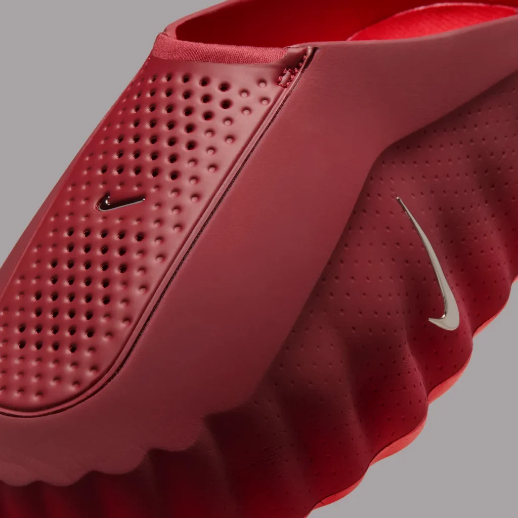 Close-up of the Nike Mind 001 “Team Red” mule showing perforated red foam upper, sculpted sidewall contours, and reflective chrome Swoosh detail