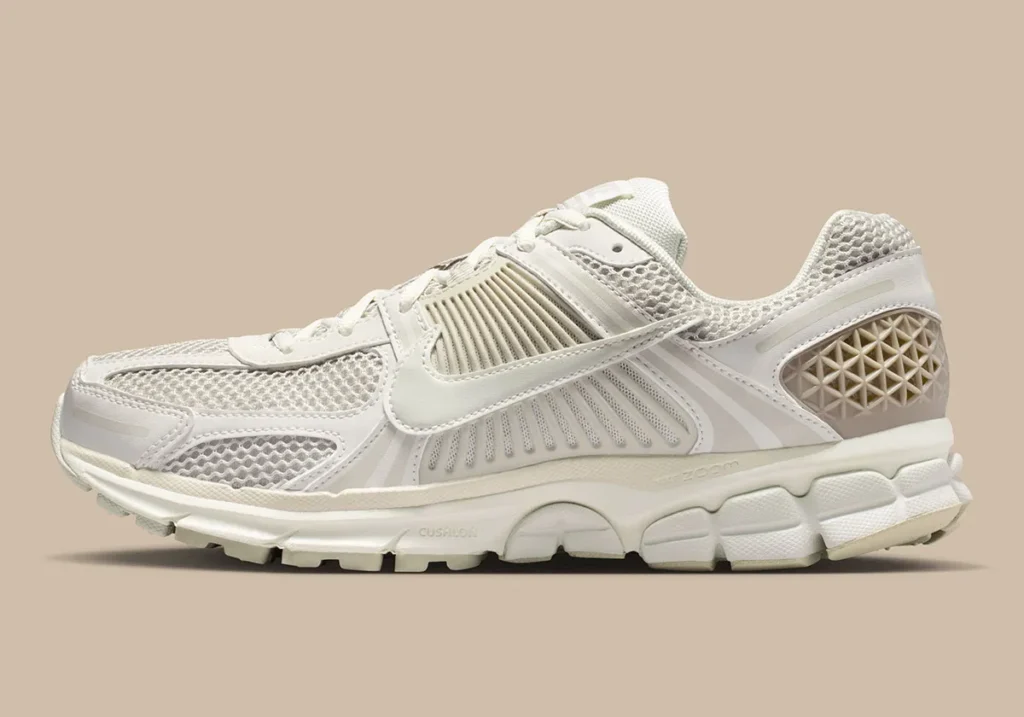 Side profile of the Nike Zoom Vomero 5 “Phantom” in soft neutral tones, featuring breathable mesh panels, layered synthetic overlays, and a sculpted Cushlon midsole with Zoom Air cushioning, set against a muted beige backdrop