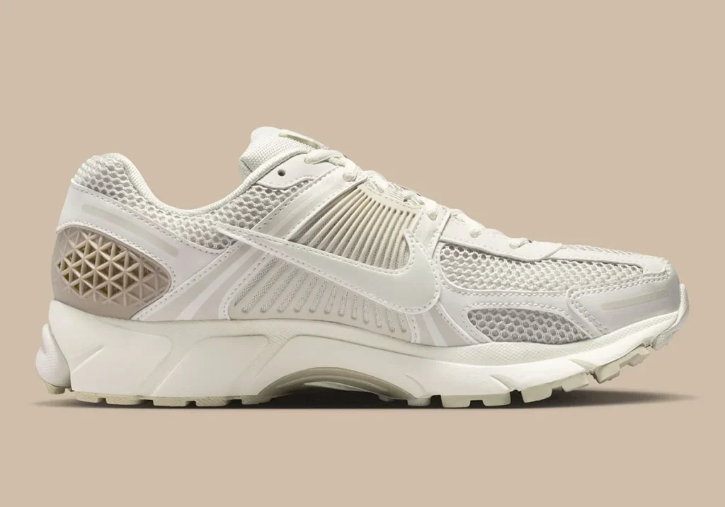 Side profile of the Nike Zoom Vomero 5 “Phantom,” highlighting layered mesh construction, tonal synthetic overlays, and sculpted midsole cushioning in soft cream and sail hues against a neutral backdrop