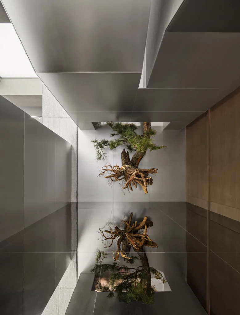Nature-inspired installation inside the On Running flagship store at MixC World featuring an elevated tree root sculpture reflected on a polished floor beneath geometric metallic ceiling panels