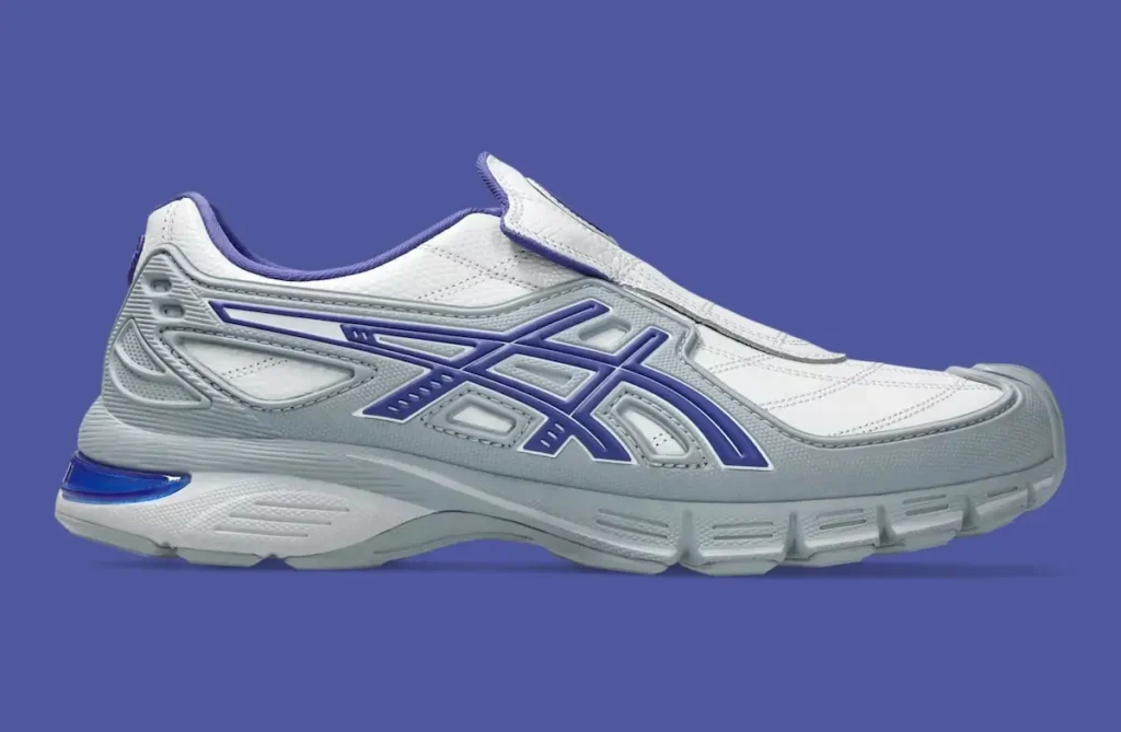 Side profile of the OTTO 958 x ASICS Gel-SD Arzachotto in white, grey, and blue, featuring a quilted stitched upper, laceless slip-on construction with an extended tongue flap, bold blue ASICS Tiger Stripes, and a sculpted midsole with segmented cushioning and a visible blue heel insert.