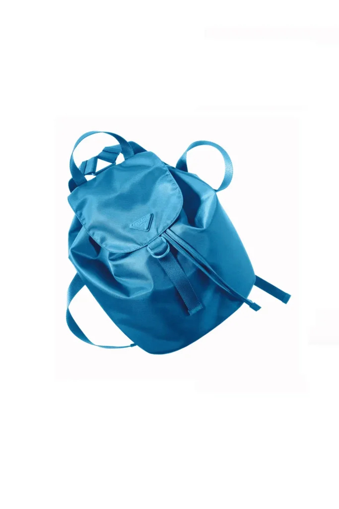 Baltic-blue recycled nylon backpack from the Prada Re-Nylon SEA BEYOND capsule, featuring a drawstring closure with flap top, adjustable shoulder straps, top carry handle, and the signature triangular Prada logo plaque on the front