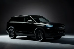 Three-quarter front view of the Jaecoo 7 SUV in a dark studio, finished in black with illuminated LED headlights, a vertical-slat grille, and shadowed body lines emphasizing its boxy, refined silhouette