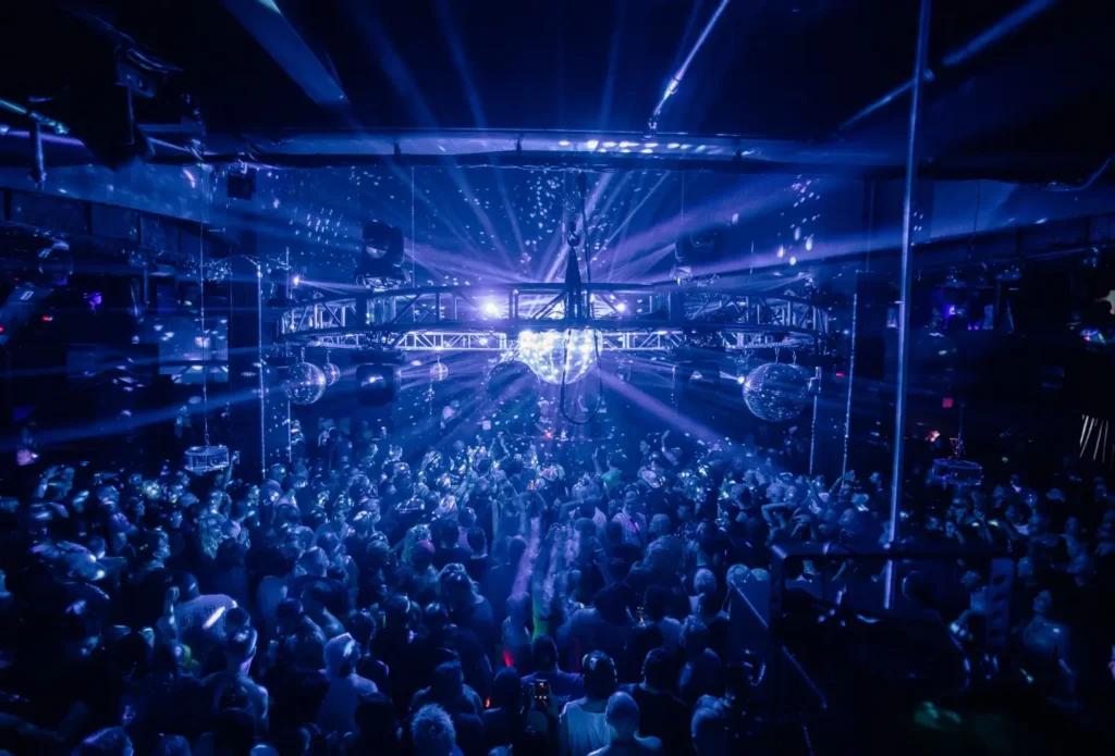 Packed nightclub crowd dancing beneath blue lights and mirrored disco balls during Twilo’s reunion event in New York City