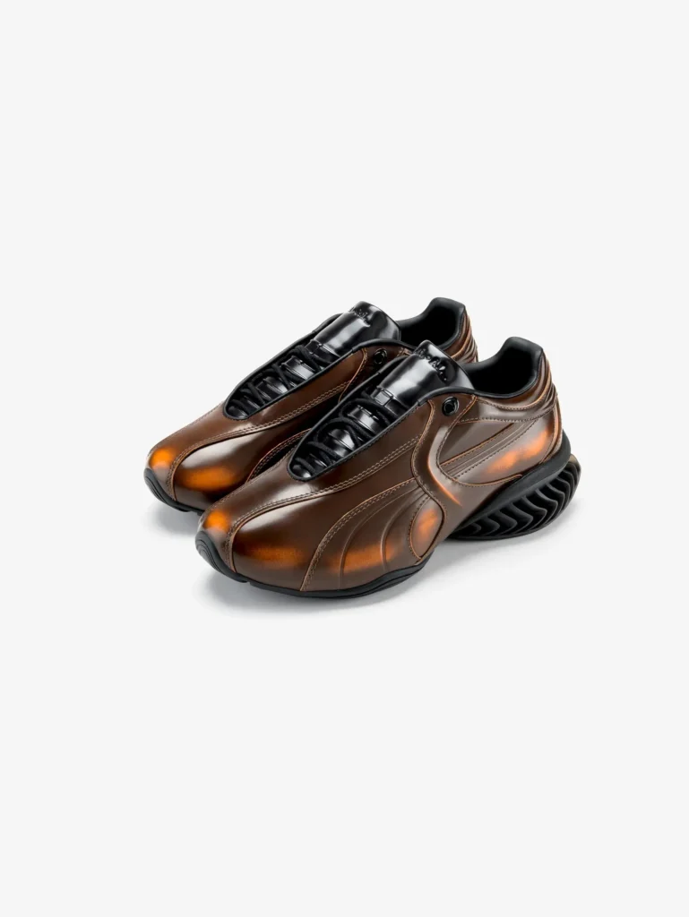 PUMA x J.L-A.L sneakers in a rich ombré brown patent leather finish, featuring a sleek low-profile design, concealed lacing system, and sculptural CELL sole, set against a clean neutral background