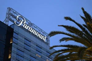Paramount logo displayed atop a modern office building at dusk, with palm tree fronds visible in the foreground against a blue evening sky