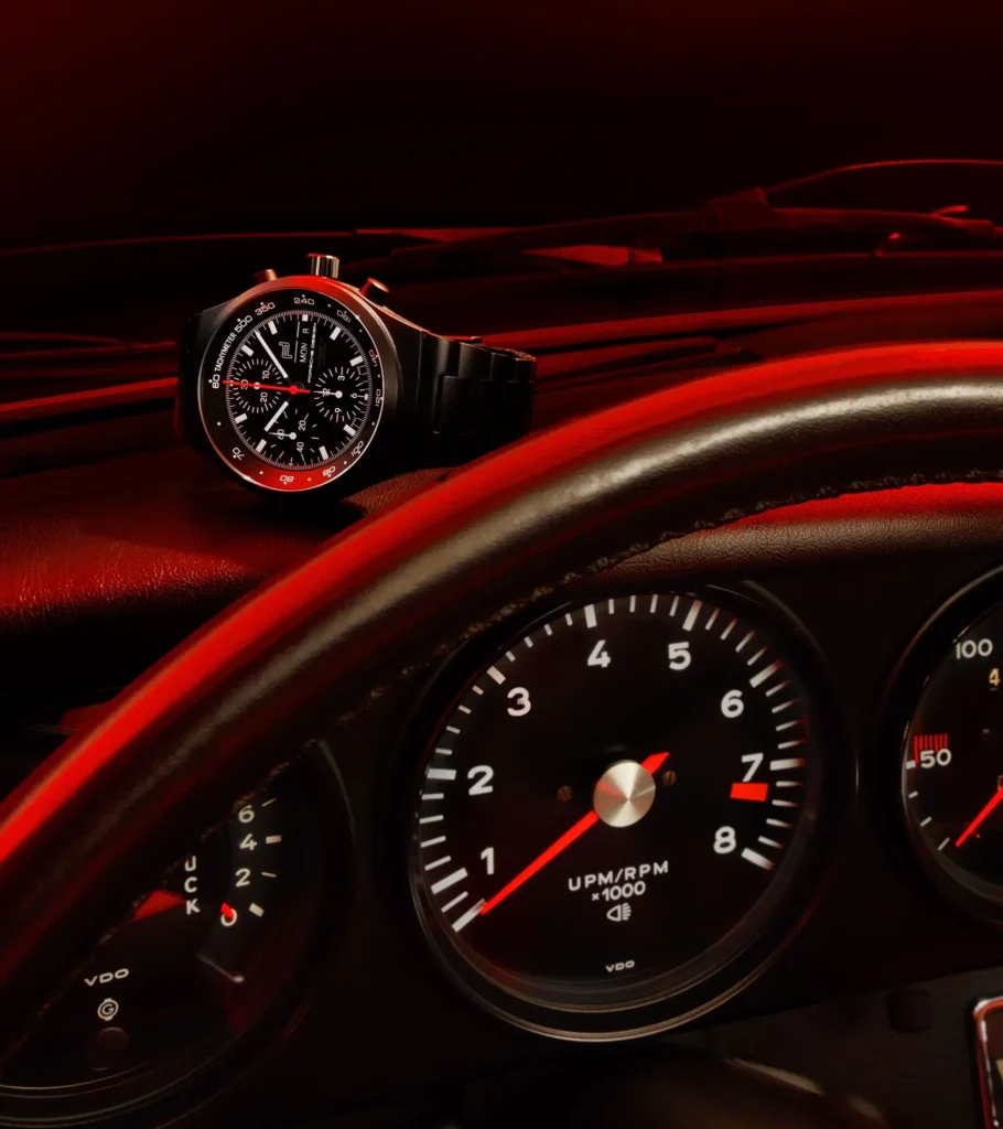 Porsche Design Chronograph 1 All Black Numbered Edition placed on a Porsche dashboard under red ambient lighting, echoing analog tachometer gauges and reinforcing the watch’s design connection to classic sports car instrumentation