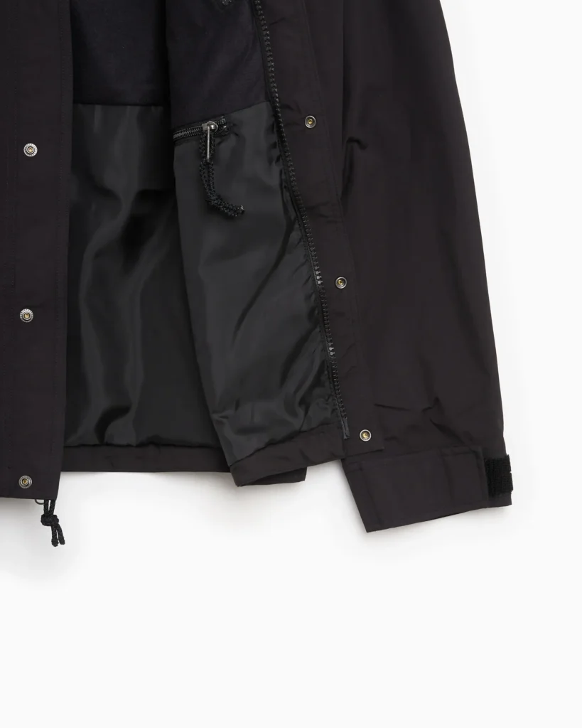Close-up of black The North Face rain jacket showing snap-button and zip front closure, inner zip pocket with cord pull, and adjustable Velcro cuff detail