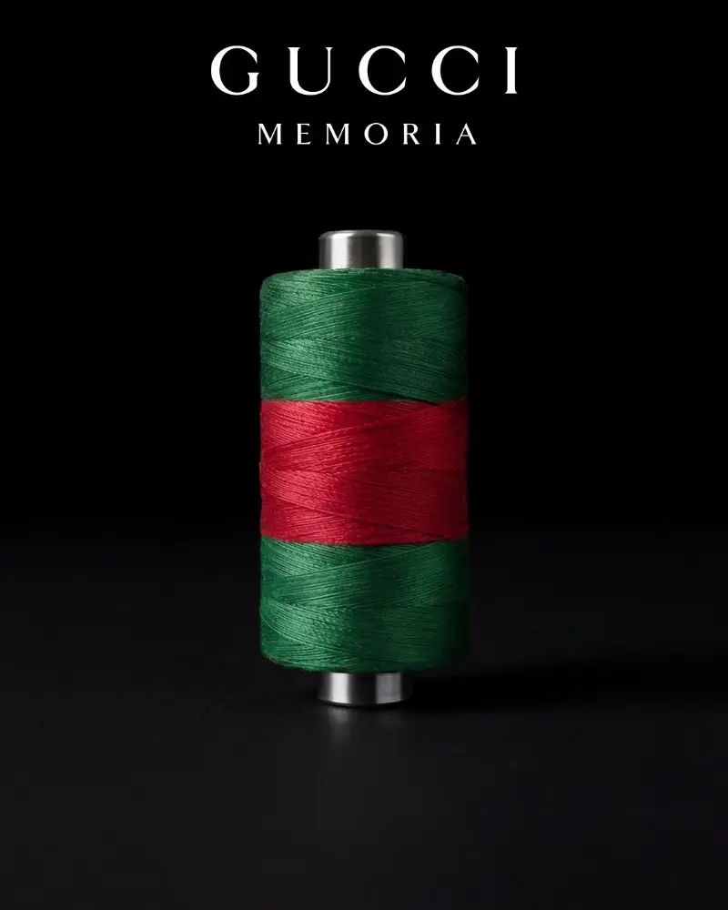 Gucci Memoria visual featuring a cylindrical spool wrapped in green and red thread, centered against a black background, symbolizing the house’s heritage through material, craft, and the interwoven continuity of its iconic color codes