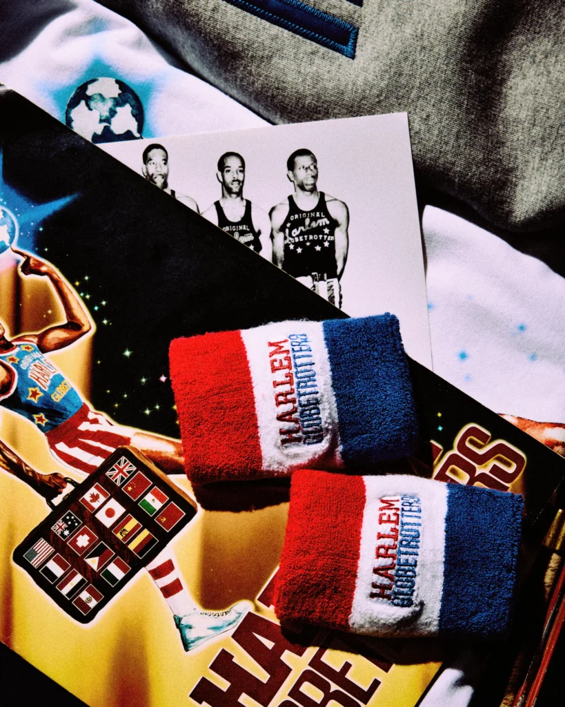 Close-up of OVO x Harlem Globetrotters accessories featuring red, white, and blue wristbands embroidered with “Harlem Globetrotters,” styled over vintage team imagery, international flag graphics, and archival basketball visuals
