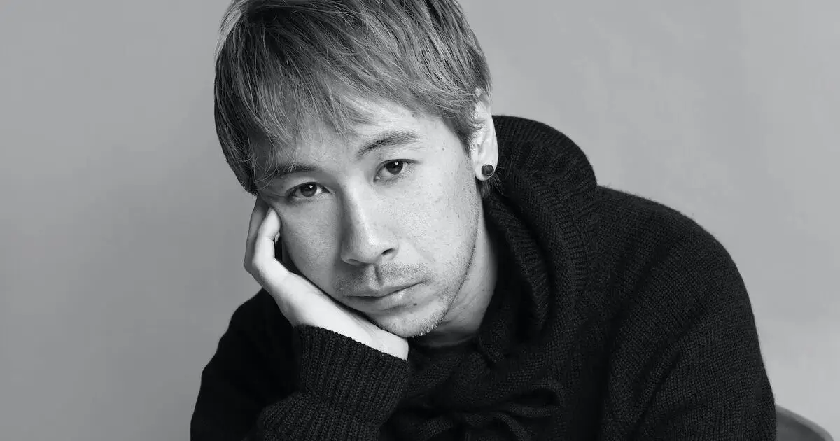 Black-and-white portrait of Jun Takahashi with short, textured hair resting his head on his hand, gazing directly at the camera with a contemplative expression, wearing a dark knit sweater against a minimal, softly lit background