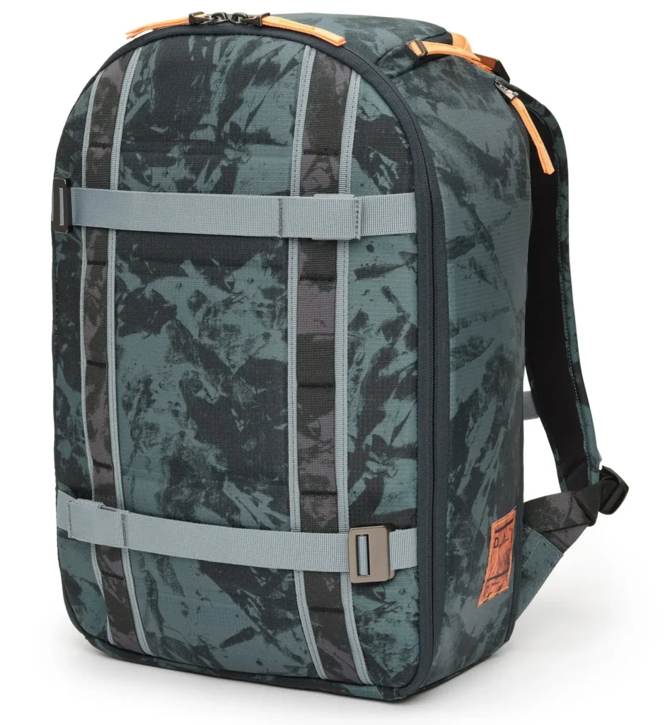 A three-quarter front view of a structured teal-green backpack with a tonal camo-style pattern, emphasizing its rounded, semi-rigid silhouette. The front panel is organized with vertical webbing columns intersected by two horizontal compression straps, each secured with metal adjusters, reinforcing its modular, utility-driven design. Subtle orange accents appear along the top zipper and pull tabs, adding contrast to the otherwise muted palette. The side profile reveals a clean, slightly tapered structure with a secondary zip compartment and a small leather patch detail near the base, introducing a refined branding element. The materials appear durable and lightly textured, suggesting water resistance and everyday resilience. Overall, the design balances technical function with a contemporary urban aesthetic, positioned between outdoor gear and city-ready carry