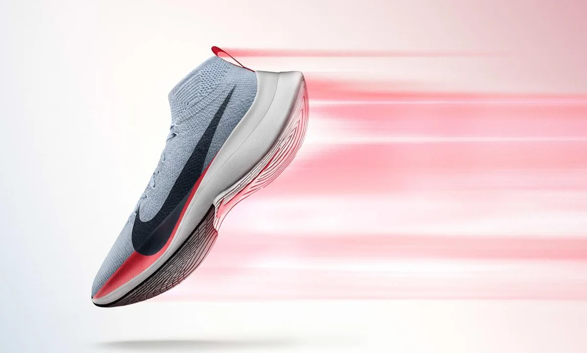 Nike running shoe in grey with black Swoosh and red accents shown in motion with blurred red speed trails against a clean white background, emphasizing lightweight performance and speed