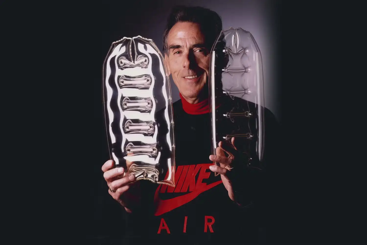 Portrait of a Nike designer holding early transparent Air cushioning prototypes, showcasing the internal structure of visible Air units against a dark studio background