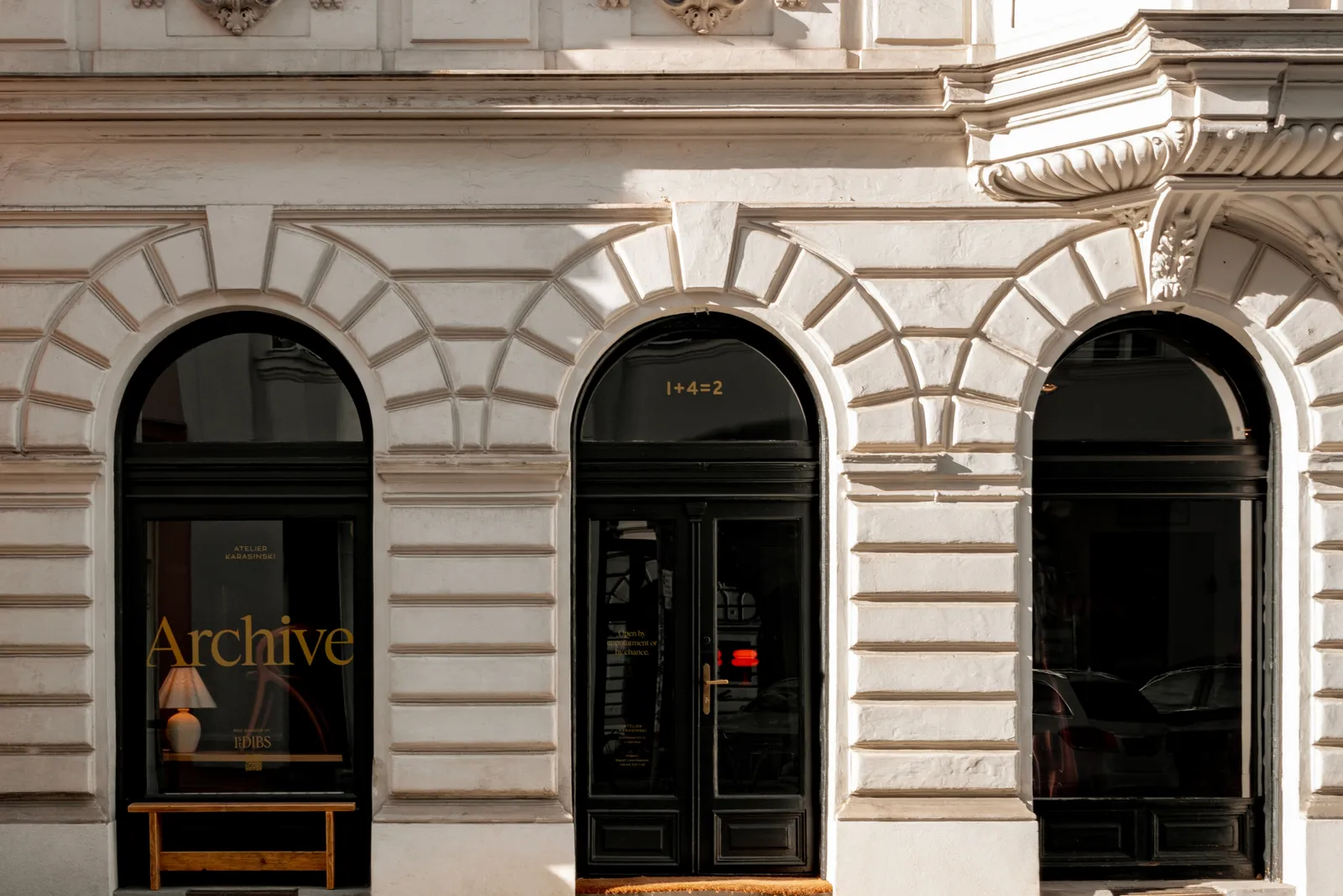Exterior of Atelier Karasinski Archive with arched windows, classical stone façade, and black-framed entrance featuring subtle gold typography and interior glimpse