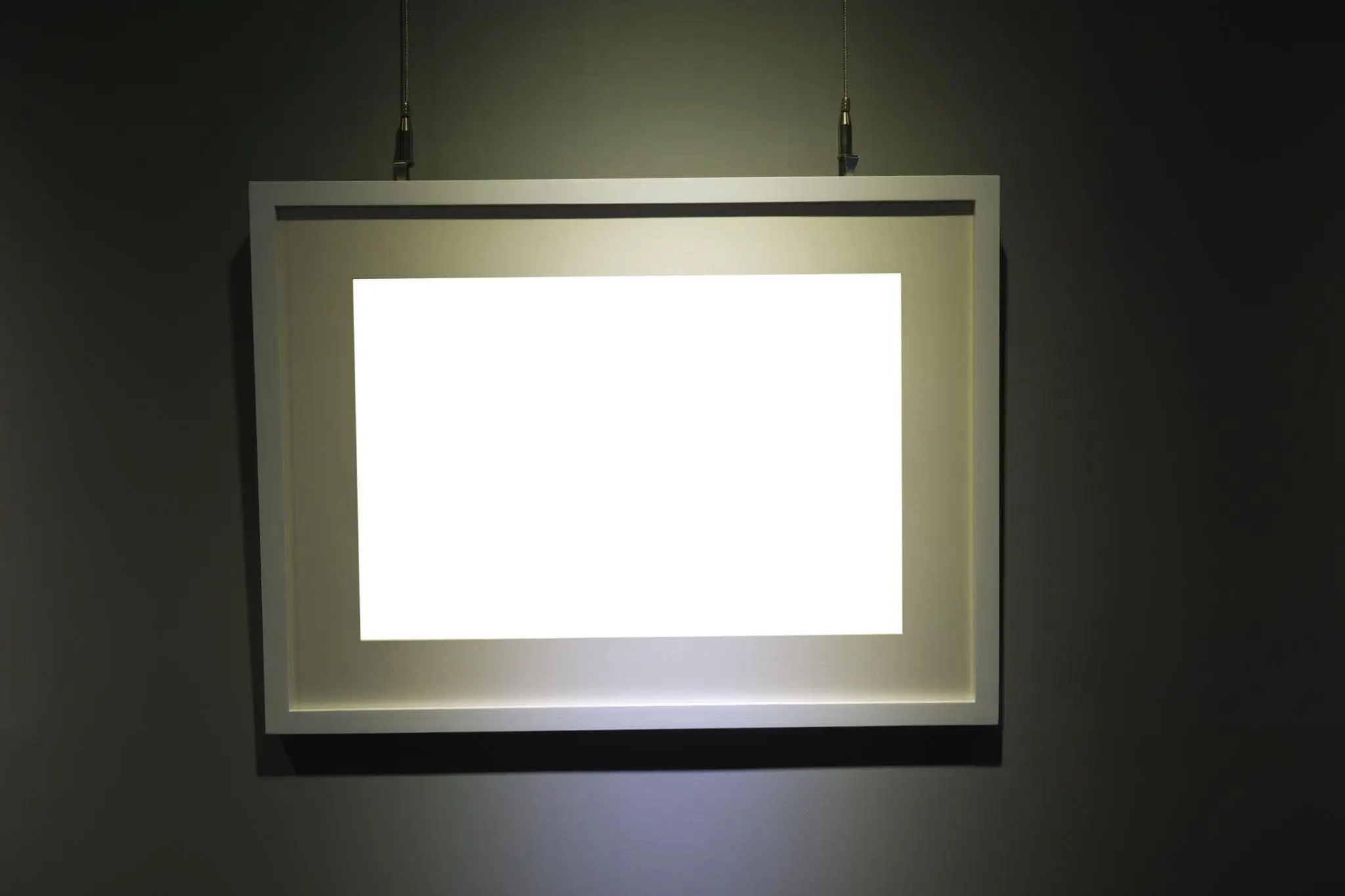 Minimalist illuminated rectangular light panel suspended against a dark wall, casting a soft glow around its frame