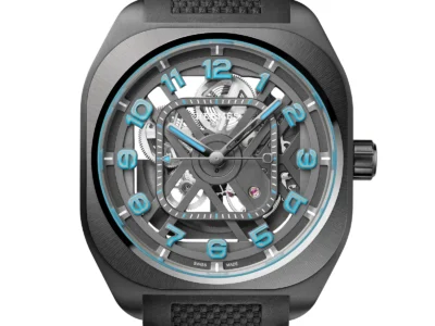 Skeletonized Hermès H08 wristwatch in matte black PVD-coated titanium, featuring an open-work dial that reveals the mechanical movement beneath, with bold blue Arabic numerals around the chapter ring, luminous hands, a geometric cushion-shaped case, and a textured black rubber strap against a clean white background